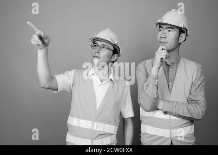 Zwei junge asiatische Männer Bauarbeiter zusammen vor grauem Hintergrund Stockfoto