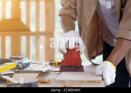 Alter Mann verwenden rote elektrische Hobel, um die Oberfläche des Holzbretts in der Schreinerei zu glätten. Stockfoto