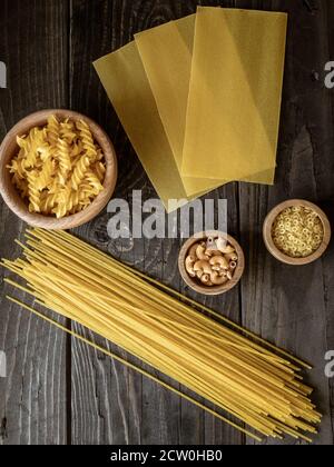 Verschiedene Arten von Pasta auf dunklem Holztisch. Spaghetti, Lasagne, Fusilli. Overhead-Aufnahme mit Copyspace. Stockfoto