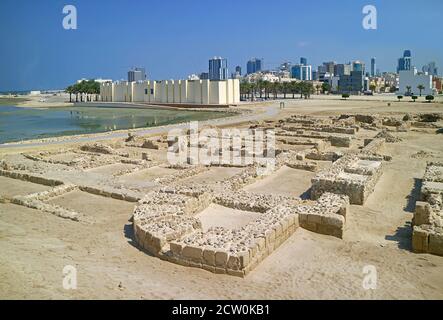 Überreste von Qal'at al-Bahrain oder Bahrain Fort Struktur mit seinem Museum und Manama Moderne Stadtbild im Hintergrund, Manama, Bahrain Stockfoto