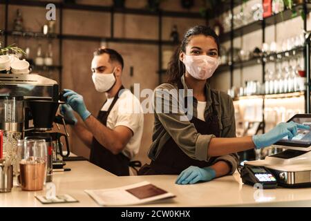 Zwei Baristas mit medizinischer Maske, die Kaffee hinter der Theke servieren Während der Quarantäne in Innenräumen Stockfoto