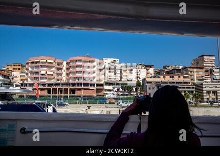 Adria Blick auf Saranda Stadt und Resort, Albanien, von der Fähre, die nach Korfu, Kerkira, Griechenland segelt gesehen. Silhouette einer unerkennbaren jungen Frau, die Fotos von der Szene Stockfoto