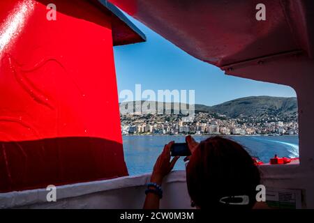 Adria Blick auf Saranda Stadt und Resort, Albanien, von der Fähre, die nach Korfu, Kerkira, Griechenland segelt gesehen. Silhouette einer unerkennbaren jungen Frau, die Fotos von der Szene Stockfoto
