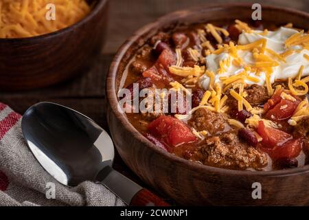 Nahaufnahme einer Schüssel Chili con Carne mit geschreddertem Cheddar Käse und Sauerrahm Stockfoto