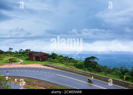 Khmer Familie fährt Motorrad auf der Berg Asphaltstraße an einem regnerischen Tag, bedeckt bewölkt den Golf im Hintergrund. Kampot, Süd-Kambodscha. Stockfoto