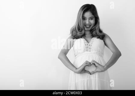Studio Schuss von jungen glücklich asiatische schwangere Frau lächelnd und Macht Hand Herz Zeichen in ihrem Bauch Stockfoto