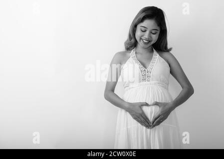 Glücklich junge asiatische schwangere Frau lächeln, während die Hand Herz unterzeichnen Sie auf ihrem Bauch mit Liebe für ihr Baby Stockfoto