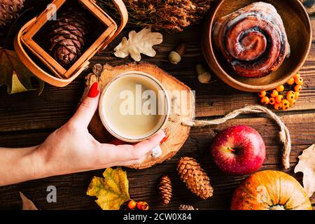 Weibliche Hände halten heißen Kaffee, Herbstblätter auf einem alten hölzernen Hintergrund. Vintage. Herbsturlaub Konzept Stockfoto