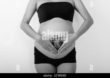 Junge asiatische schwangere Frau hält Sonogramm ihres Babys während Hand Herz Zeichen machen Stockfoto