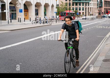 LONDON, ENGLAND - 24. JULI 2020: Junger asiatischer männlicher Deliveroo-Kurierfahrer bei einer Mittagslieferung während der COVID-19-Coronavirus-Pandemie - 1 Stockfoto