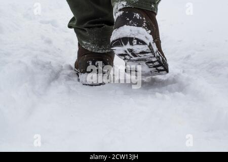 Männliche Füße in Stiefeln, die im Winterschnee entlang laufen Stockfoto