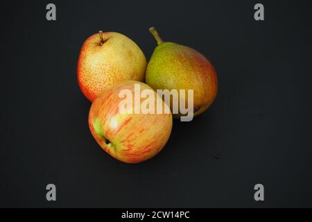 Reife Früchte auf schwarzem Hintergrund. Zwei schöne Birnen und ein Apfel. Stockfoto