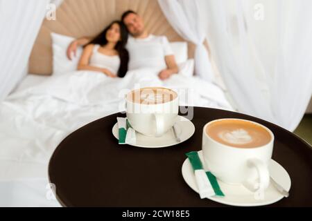 Zimmerservice bringt 2 Tassen Kaffee ins Hotel Zimmer für ein Ehepaar, das in einem Bett im liegt Morgen Stockfoto