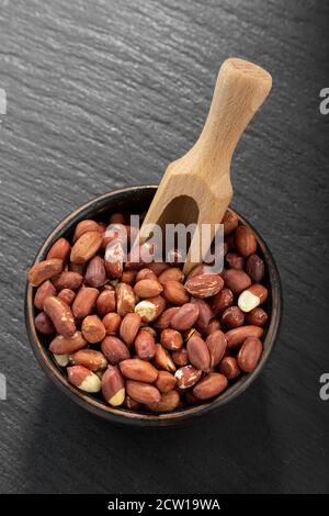 Geschälte Erdnüsse in einer Tonschüssel auf einem schwarzen Tisch. Stockfoto