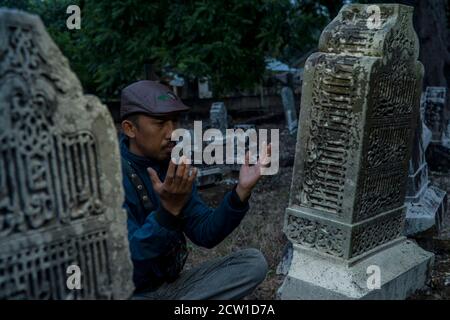 Ein Mann, der in einer alten Grabanlage im Königreich Samudra Pasai in der Abenddämmerung in Geudong, Samudra District, Aceh Utara, Indonesien, betet Stockfoto