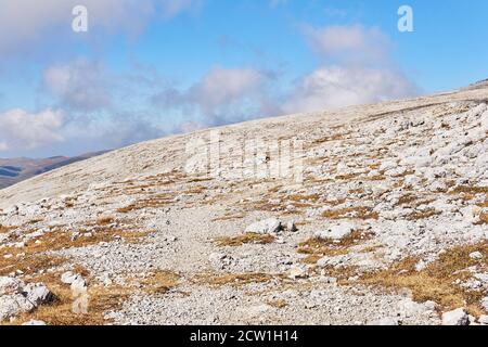 alpine Berghang mit trockenem Gras und weißen Steinen bedeckt Stockfoto