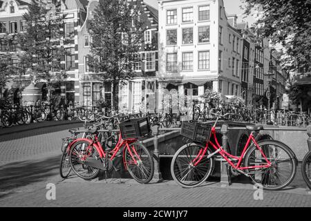 Ein Bild von zwei roten Rädern auf der Brücke über den Kanal in Amsterdam. Der Hintergrund ist schwarz-weiß. Stockfoto