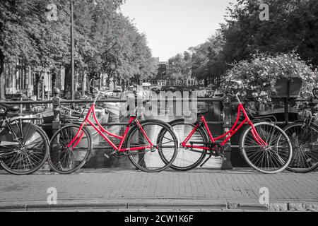 Ein Bild von zwei roten Rädern auf der Brücke über den Kanal in Amsterdam. Der Hintergrund ist schwarz-weiß. Stockfoto