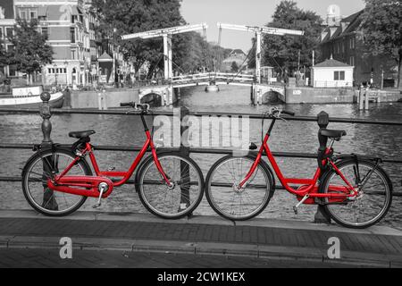 Ein Bild von zwei roten Rädern auf der Brücke über den Kanal in Amsterdam. Der Hintergrund ist schwarz-weiß. Stockfoto