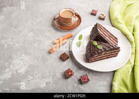 Hausgemachte Schokoladenkuchen mit Milchcreme und einer Tasse Kaffee auf einem grauen Beton-Hintergrund mit grünem Textil. Seitenansicht, Kopierraum. Stockfoto
