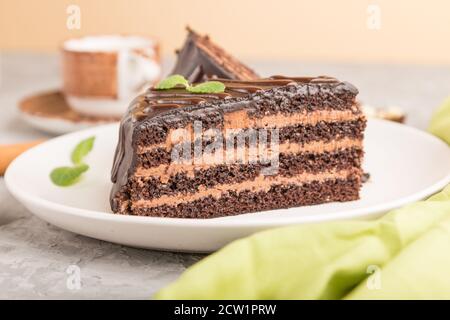 Hausgemachte Schokoladenkuchen mit Milchcreme und einer Tasse Kaffee auf grauem Beton-Hintergrund mit grünem Textil. Seitenansicht, Nahaufnahme, selektiver Fokus. Stockfoto