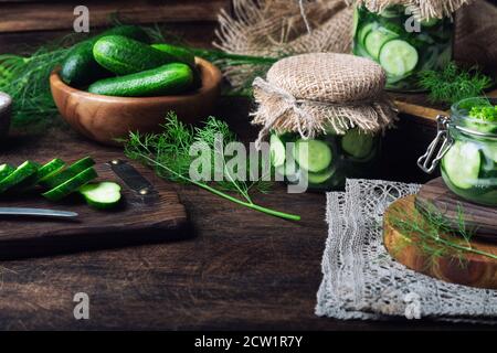 Gläser mit hausgemachten eingelegten Gurken in Scheiben geschnitten mit Dill und Knoblauch auf rustikalem Holzhintergrund. Gemüse für den Winter ernten. Stockfoto