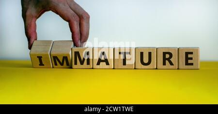 Hand dreht einen Würfel und ändert den Ausdruck "unreif" in "mature". Schöner gelber Tisch, weißer Hintergrund, Kopierraum. Geschäftskonzept. Stockfoto