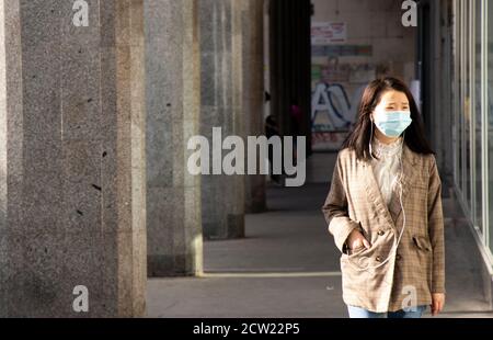 Belgrad, Serbien - 26. September 2020: Junge asiatische Frauen mit Gesichtsmaske und Ohrhörern gehen die Straße entlang mit einer Hand in einer Tasche Stockfoto