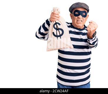 Senior gutaussehender Mann trägt Einbrechermaske hält Geldbeutel verärgert und frustriert Schreien vor Wut, schreien verrückt vor Wut und Hand angehoben Stockfoto