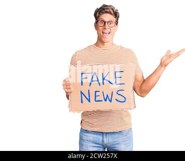 Junger hübscher Mann mit gefälschtem Nachrichtenbanner, der den Sieg feiert Glückliches Lächeln und Ausdruck des Gewinners mit erhobenen Händen Stockfoto