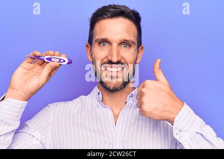 Junger schöner Mann Controlling Temperatur halten Thermometer über lila Hintergrund lächelnd glücklich und positiv, Daumen nach oben tun ausgezeichnet und approva Stockfoto