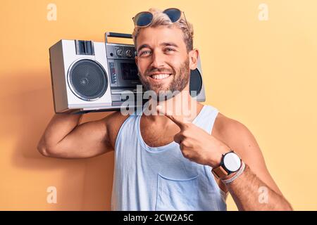 Junger, schöner blonder Mann mit Bart, der eine Sonnenbrille trägt Musik mit Boombox lächelnd glücklich zeigen mit Hand und Finger Stockfoto