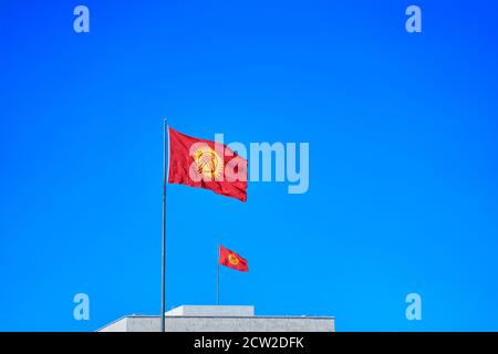 Zwei Kirgisistan Fahnen winken im Wind gegen blauen Himmel zusammen. Diplomatie Konzept, internationale Beziehungen, Patriotismus. Symbol des Staates. Stockfoto