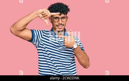 Junger arabischer Mann trägt Freizeitkleidung und Brille lächelnd machen Rahmen mit Händen und Fingern mit glücklichen Gesicht. Kreativität und Fotografie Konzept. Stockfoto