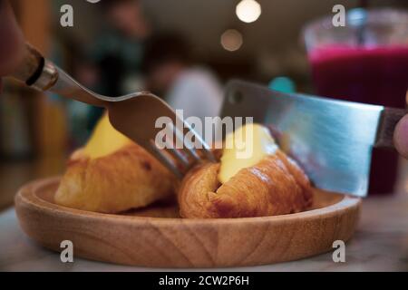 Person, die ein Stück Croissant mit Messer und Gabel isst Im Café Stockfoto