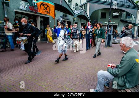 Ein alter Mann sitzt auf einer Bank und beobachtet die XR (Extinction Rebellion) Modelle, die während der Demonstration vor ihm vorbeigehen.das Label wird von anonymen und egofreien Rebellen gemacht, Klimaaktivisten von Extinction Rebellion. Inklusivität und Vielfalt sind das, wofür das Label steht. Das Label wurde während der Feier der Dutch Sustainable Fashion Week ins Leben gerufen und zählte mit rund 18 Kreationen. Durch Nopulenz bringt Extinction Rebellion Besorgnis über Mode in der Mode zum Ausdruck. Während Kleidung nicht zum Verkauf steht, werden sie für Aktivisten zur Verfügung stehen. Stockfoto