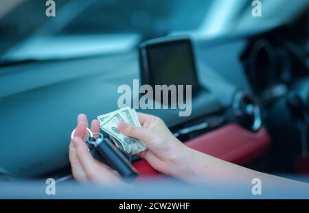 Nahaufnahme Hand asien Frau sitzt in ihrem neuen weißen Auto zeigt Schlüssel, hält Dollar Persönliche Transport Kaufkonzept Stockfoto