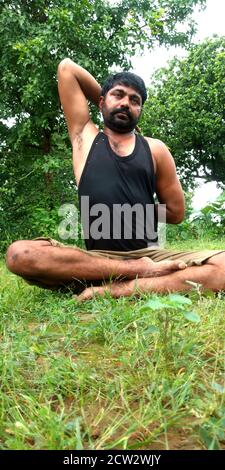 DISTRIKT KATNI, INDIEN - 05. AUGUST 2019: Ein indischer Dorfbart Junge tut Gesundheit Training in Shorts auf grünen horizontalen Land Wald Hintergrund. Stockfoto