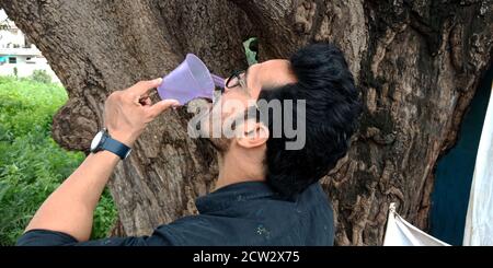 DISTRIKT KATNI, INDIEN - 12. SEPTEMBER 2019: Ein indischer Stadtmensch trinkt Wasser in der Nähe des Baumes. Stockfoto