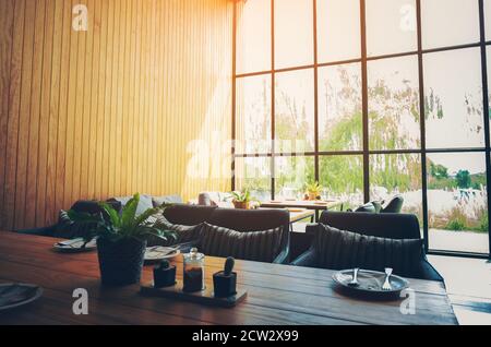 Café-Interieur mit moderner und einfacher Dekoration, große Glasfenster. Morgenlicht, niemand drinnen, woodeb Tisch Stockfoto