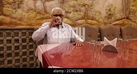 DISTRIKT KATNI, INDIEN - 15. SEPTEMBER 2019: Ein indischer alter Mann trinkt Wasser auf Restauranttisch. Stockfoto