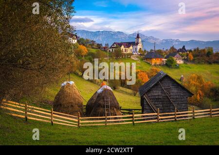 Schöne Landschaft im Herbst und bunte Laubbäume auf den Hügeln. Haystacks und Holzhütte im Garten bei Sonnenuntergang, Karpaten, Trans Stockfoto