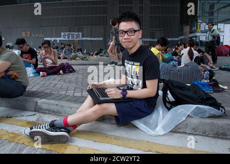 Hongkong, Hongkong, China. Oktober 2014. Die Umbrella Revolution von 2014, Roney Chan 20, sitzt bei seiner Arbeit an der Universität auf seinem Computer in der geschlossenen Straße Protestzone auf der Harcourt Straße vor den Regierungsbüros. Er trägt das gelbe Band, gleichbedeutend mit der Bewegung. Quelle: Jayne Russell/ZUMA Wire/Alamy Live News Stockfoto