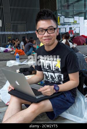 Hongkong, Hongkong, China. Oktober 2014. Die Umbrella Revolution von 2014, Roney Chan 20, sitzt bei seiner Arbeit an der Universität auf seinem Computer in der geschlossenen Straße Protestzone auf der Harcourt Straße vor den Regierungsbüros. Er trägt das gelbe Band, gleichbedeutend mit der Bewegung. Quelle: Jayne Russell/ZUMA Wire/Alamy Live News Stockfoto