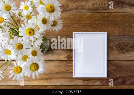 Weißer kleiner Rahmen-Mockup mit Gänseblümchen-Wildblumen. Leerer Rahmen für Präsentationsgrafiken. Schablonenrahmen für moderne Kunst Stockfoto