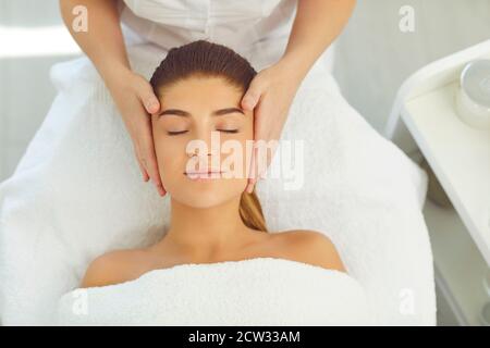 Schöne Frau bekommen Gesichtsmassage liegend mit geschlossenen Augen auf Bett im Schönheitssalon Stockfoto
