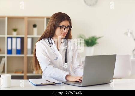 Junge Ärztin Eingabe auf Laptop Keyword Surfen Internet in Büro der modernen Klinik Stockfoto