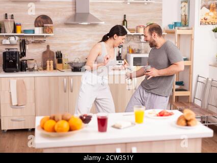 Pärchen mit Spaß in der Küche Fechten mit großen Löffeln während des Frühstücks tragen Pyjamas. Fröhlich sorglos fröhlich lustige Liebhaber, Kampf Holzlöffel, Bonding Spiel Kampf Schwertkampf, glücklicher Lebensstil Stockfoto