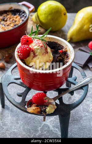 Birnenbrösel Dessert mit Schokolade, Haselnüssen, Eis und Himbeersoße Stockfoto