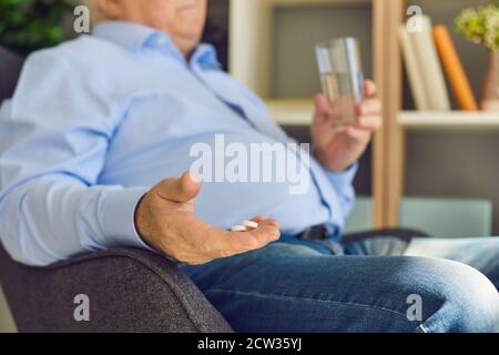 Leitender Patient, der verordnete Medikamente mit Wasser in einem sitzt Sessel zu Hause Stockfoto